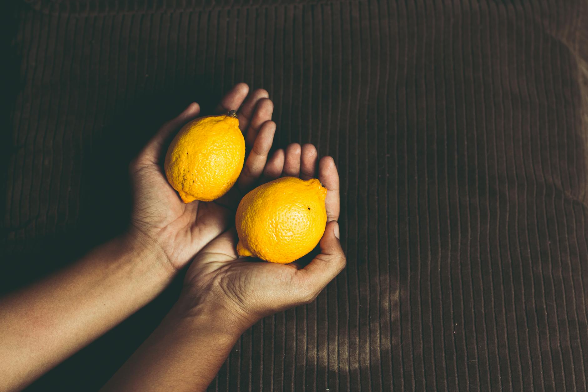 Close-up of two fresh lemons held in cupped hands on a brown surface, symbolizing the fresh sensation of lemon vibrators.