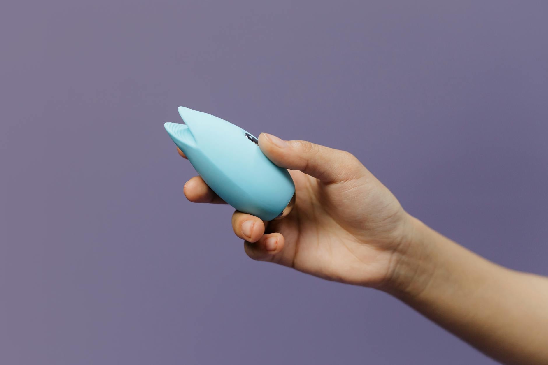 Close-up of a blue silicone vibrator held in an open hand against a purple background, representing self-pleasure and sexual wellness.