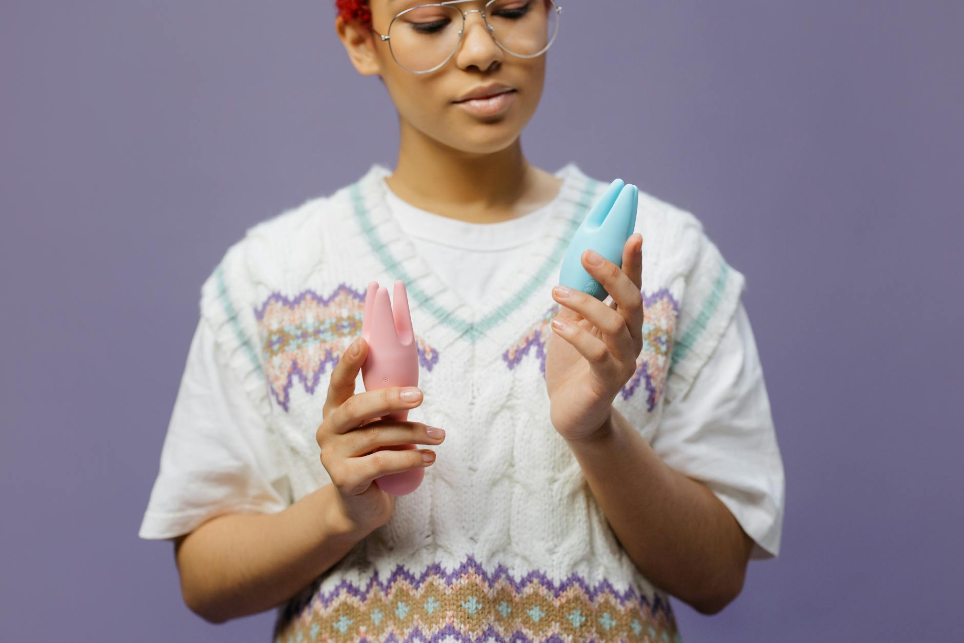 Person holding blue and pink silicone clitoral vibrators in hands