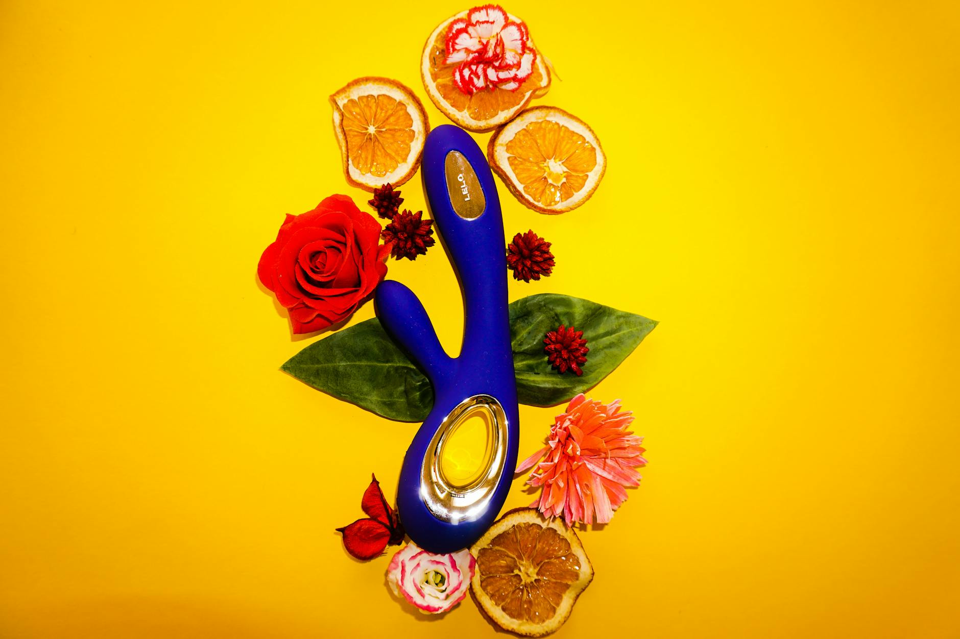 A blue lemon vibrator surrounded by fresh citrus and flowers on a yellow background